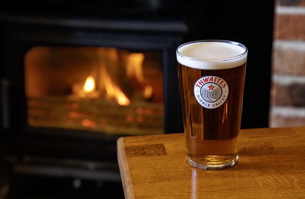 Pint of Thwaites ale beside a lit log burner